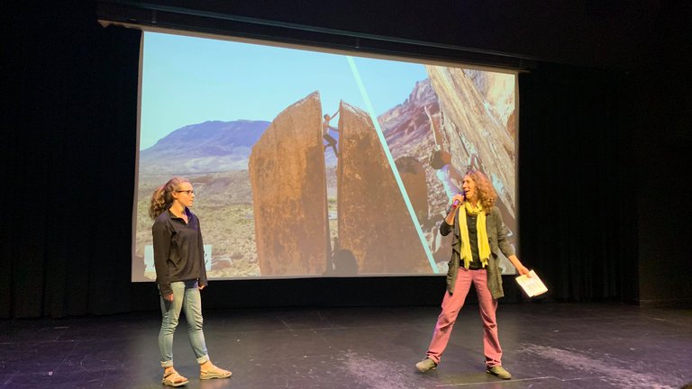 Shaelyn Silverman and Juliet Ryan-Davis MC ReelRock 14, in front of a slideshow showing people bouldering in a crack in boulder in Bishop CA.