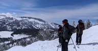 Two people on a snowy hillside look sideways toward the camera.