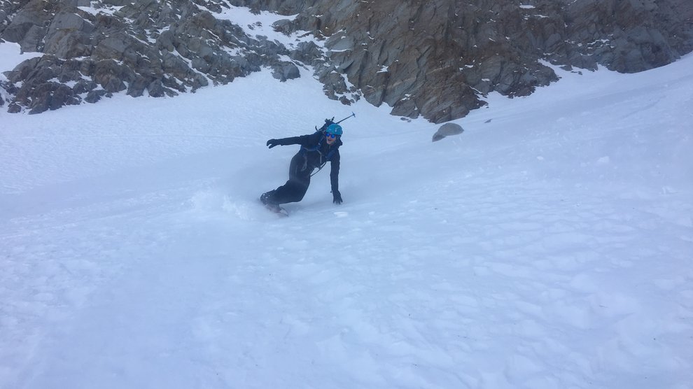 View of a snowboarder going down a snow-filled couloir.