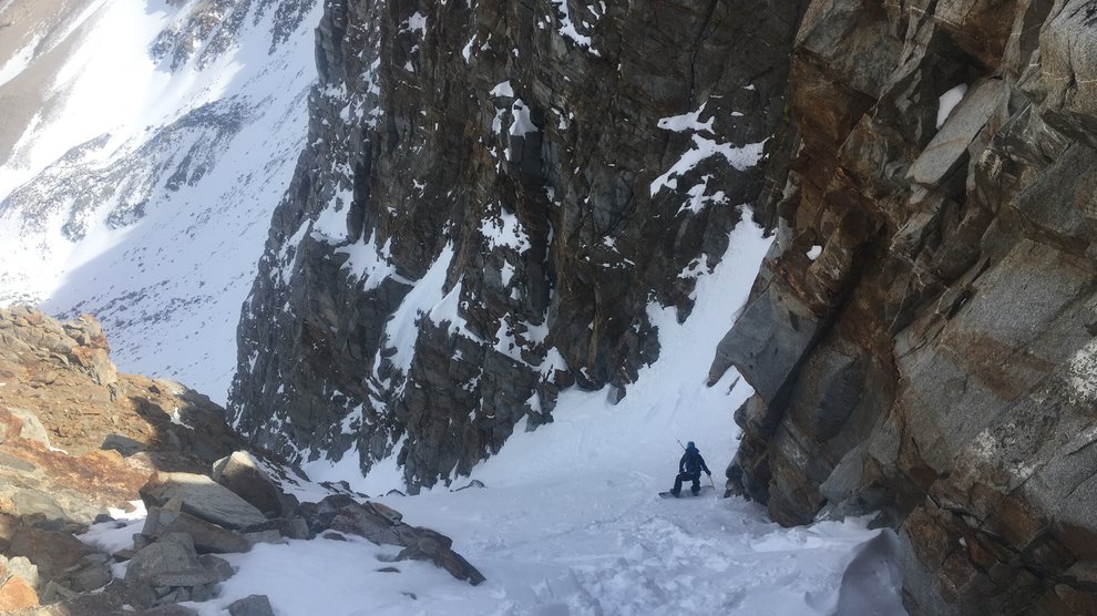 View of a very narrow, snow-filled couloir and a snowbaorder going down.