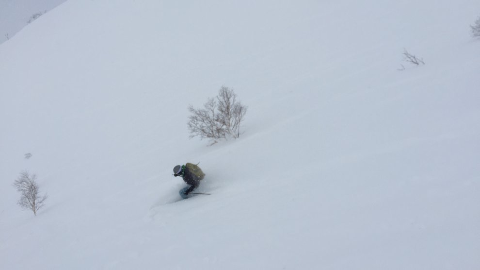View of a skier rieding down a slope in deep snow.