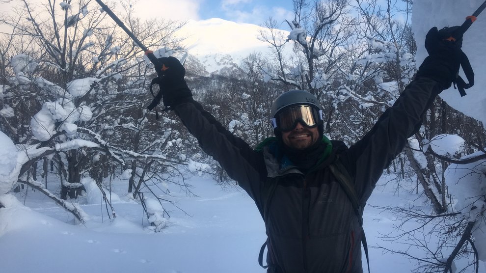 Skier standing between snow-covered trees, hands in the air, happy.