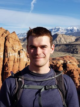Photo of Noel Csomay-Shanklin in hiking gear in a mountaineous region.