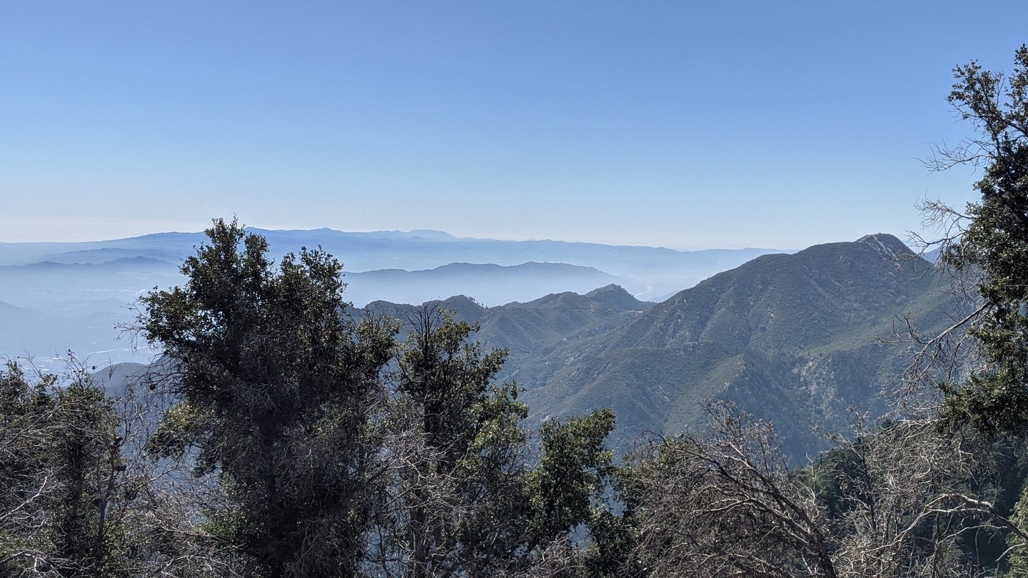 View over many rows of mountain tops, with low-lying haze in between. The mountains are covered in green vegetation.