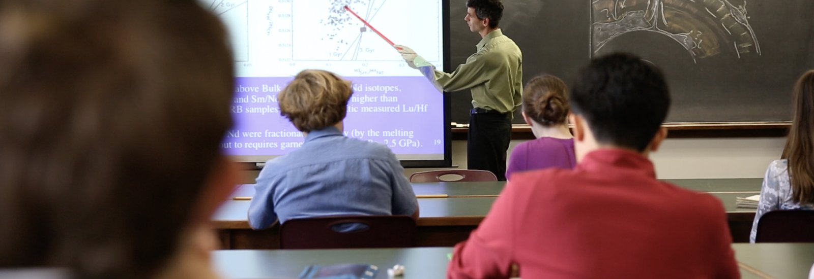 teacher pointing with stick to projected image students in foreground