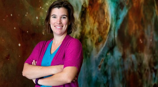 photo of woman standing with arms crossed in front of astronomy image