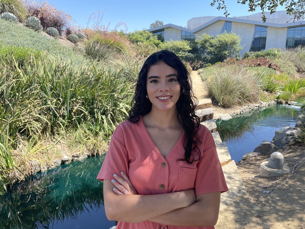 Women with hands crossed smiling in front of a river and bushes