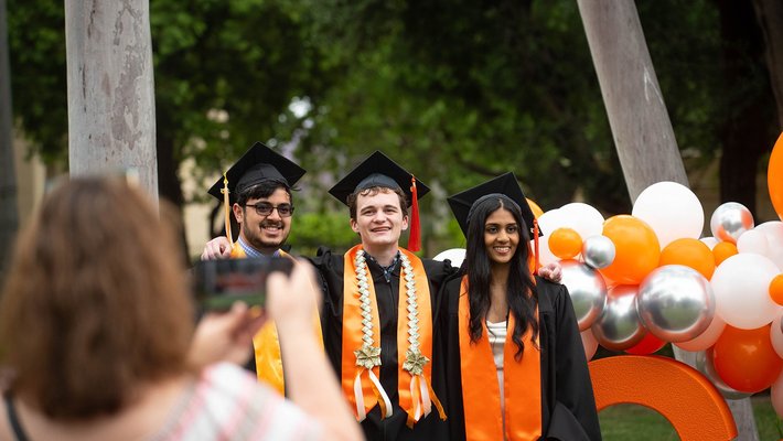Three Caltech graduates posing for a photo in front of a decorated Caltech sign