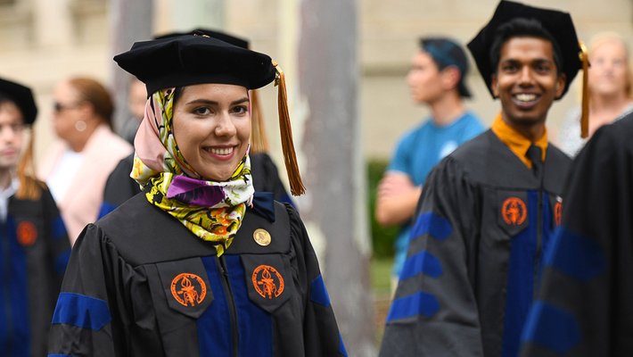 A female PhD graduate wearing a headscarf and a male PhD graduate in the background at the Commencement ceremony