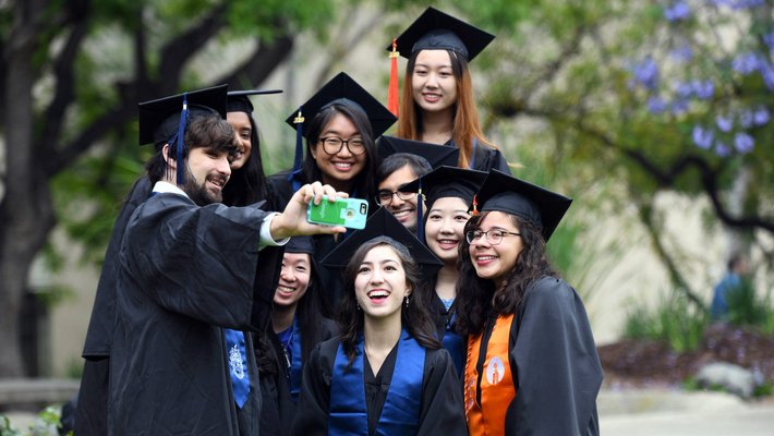 students taking a selfie in Commencement cap and gown