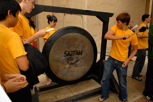 students in yellow shirts with large hanging gong