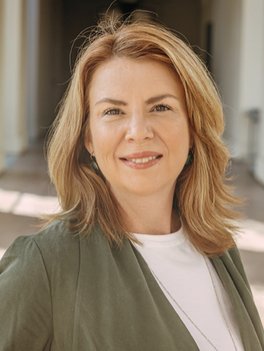 woman with blond hair and olive green jacket is smiling at the camera
