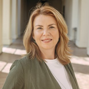 woman with blond hair and olive green jacket is smiling at the camera