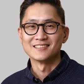 Man with dark hair and dark-rimmed glasses wearing a dark navy collared shirt and sweater