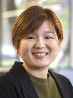 Smiling woman with brown hair wearing an olive green shirt and black suit jacket