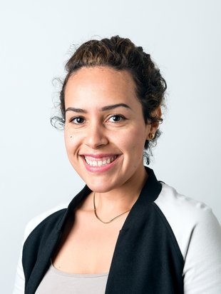 person who identifies as a women smiling. person has on a white shirt and their hair is pulled back