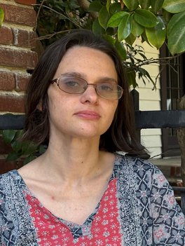 headshot of J. Bussone, dark bob blends a bit with shadow behind her, slight tint to transition lenses, red and blue Indian block print shirt