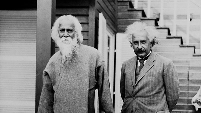 Bengali poet Rabindranath Tagore to Einstein's right, standing on the back patio of Einstein's summer home. Tagore in customary clothes, a long sleeved robe like garment. Einstein in a suit and tie, holding his pipe, squinting at the camera.