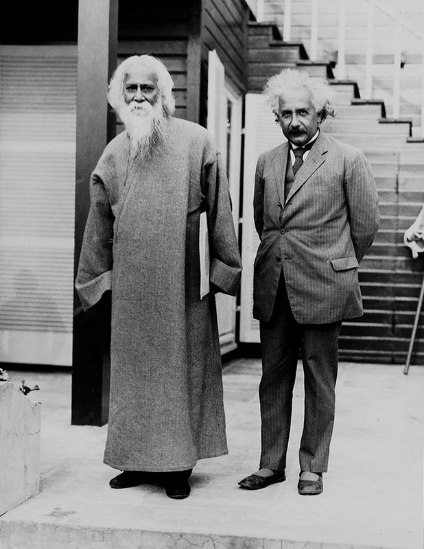 Bengali poet Rabindranath Tagore to Einstein's right, standing on the back patio of Einstein's summer home. Tagore in customary clothes, a long sleeved robe like garment. Einstein in a suit and tie, holding his pipe, squinting at the camera.