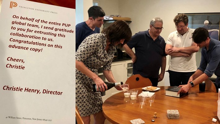 triptych of photos, D. Buchwald & J. Eisenthal open book and prosecco, respectively. Congratulatory note from PUP Director, Christie Henry to project. Editors gathered around kitchen table to see book.
