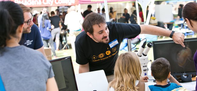 Caltech student showing event visitors a graphic on a computer screen.