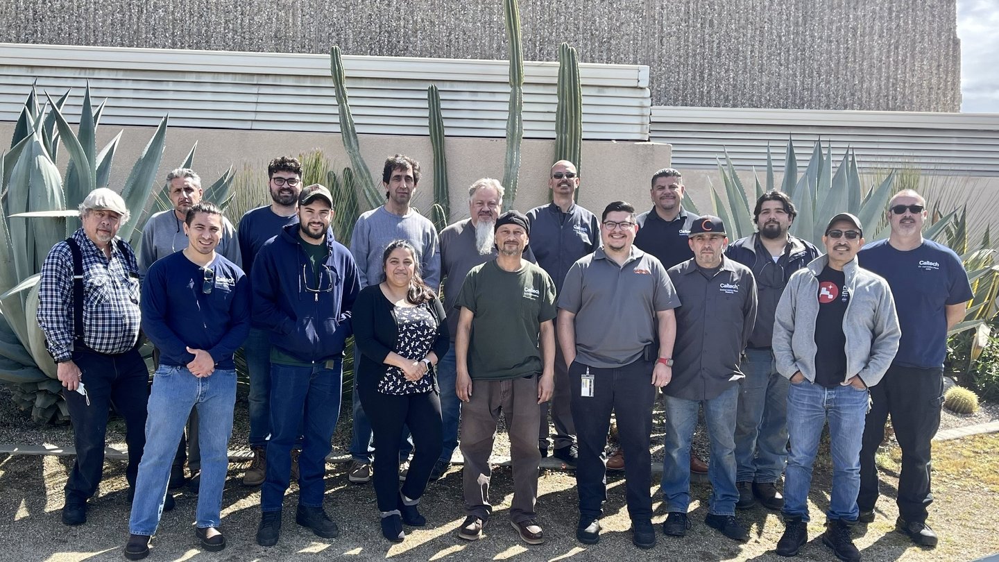 CUP Team; 16 people standing in front of central utility plant with large dessert plants behind them