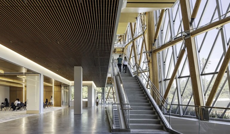 A large open space in a modern buiding features polished concrete floors, floor-to-ceiling windows, and a staircase rising to the second floor.