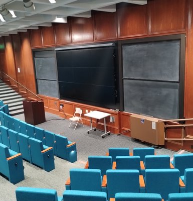 An empty lecture hall with a chalkboard and podium at the the front