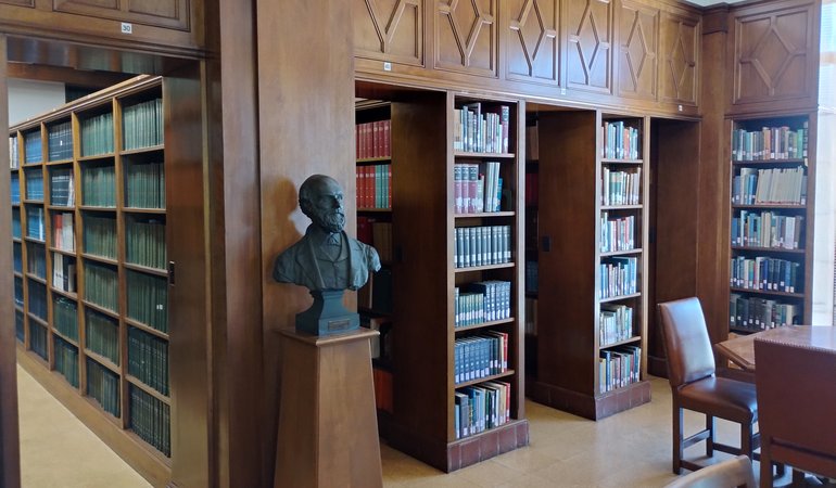 A library with shelves of books and a bust of some man on a pedestal