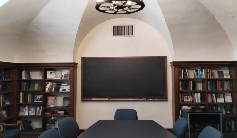 A small reading room with a center table and shelves of books against the walls.