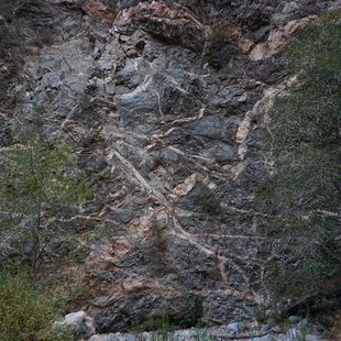 A cliff face of dark rock with pink granite dikes crosscutting, with noticeable offsets from faults through the pink layers.