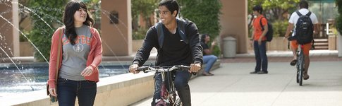A student on a bicycle talking to another student.