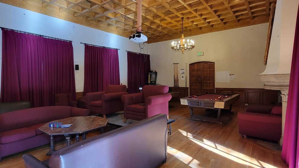 interior of Fleming House Lounge with several large couches, two large sofa chairs, a pool table, a large fireplace, and a projector mounted on the ceiling
