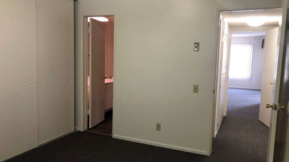 Empty bedroom with view of bathroom, hallway, and living room.