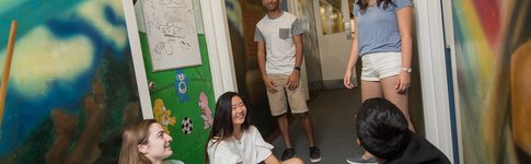 Students talking in the hall at Lloyd House. Featuring painted, colorful murals on the walls.