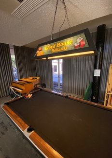 Lloyd Lounge pool table featuring piano and hanging light that says "Lloyd House Billiards."