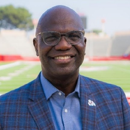 A man smiles and poses in front of a football field