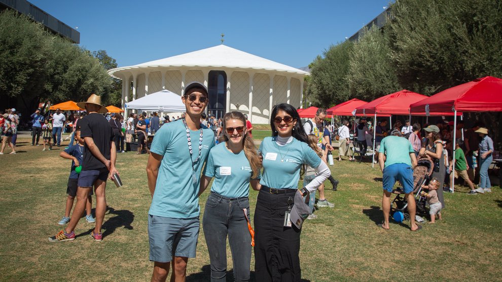 Three postdocs in blue Explore Caltech t-shirts smile and pose in front of Beckman Auditorium
