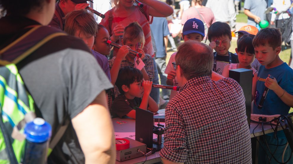 A group of children gather at a table and look through individual spectroscopes