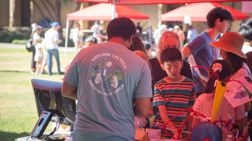 A volunteer turned around, showing the back of their t-shirt with the Explore Caltech logo