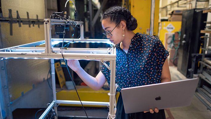 Woman with laptop in one hand examines lab equipment