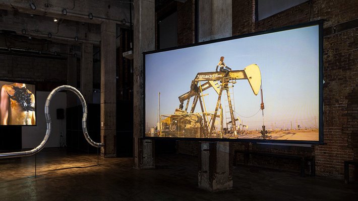 Art exhibit featuring woman riding an oil derrick