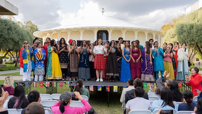 Students in multicultural attire stand on stage on Beckman Mall