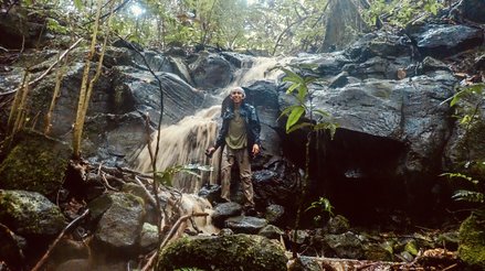 Isaac wearing rain gear in front of a waterfall