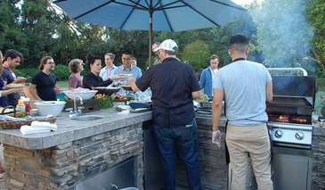 2 people cooking on a BBQ, with others standing around.