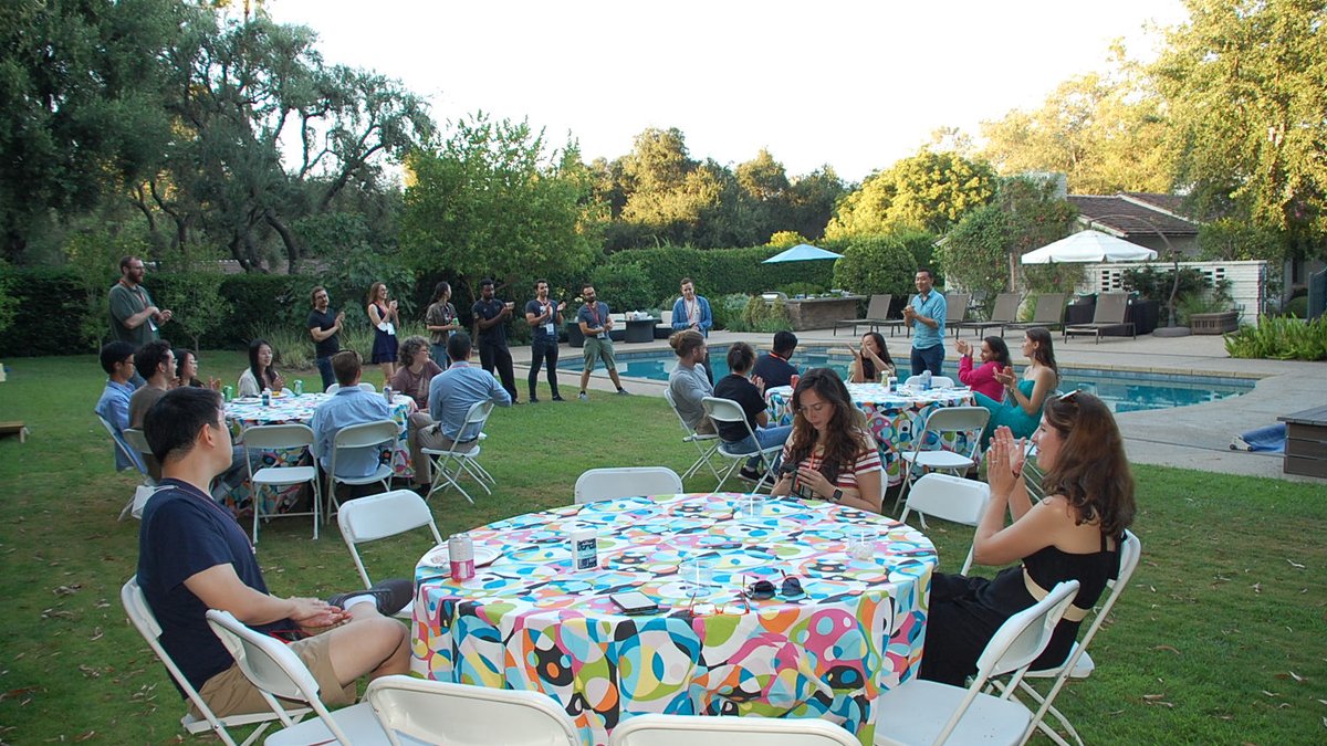 DataSAI Summer school students sitting at round tables in a garden next to a pool