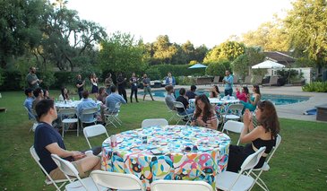 DataSAI Summer school students sitting at round tables in a garden next to a pool