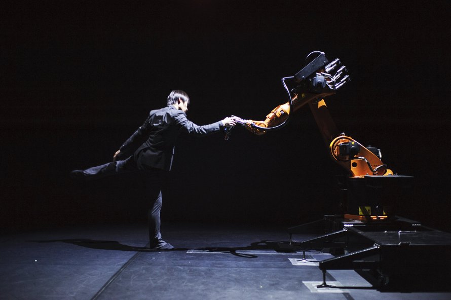 A person standing next to a robot on a dark stage