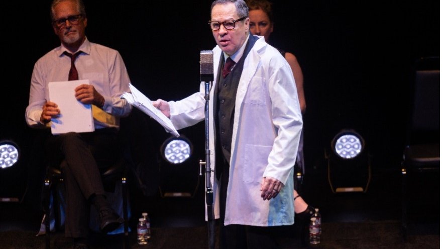 actor in front of microphone wearing white lab coat