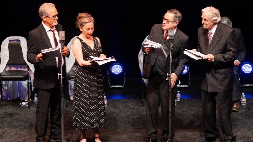 four actors on stage carrying scripts
